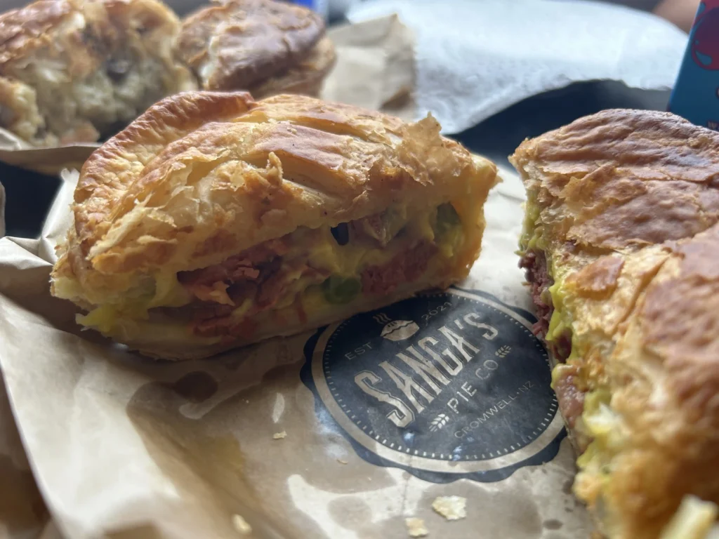 Sanga's Pies Cromwell South Island — cut open meat pie with corned beef and pea filling on branded Sanga's Pie Co wax paper