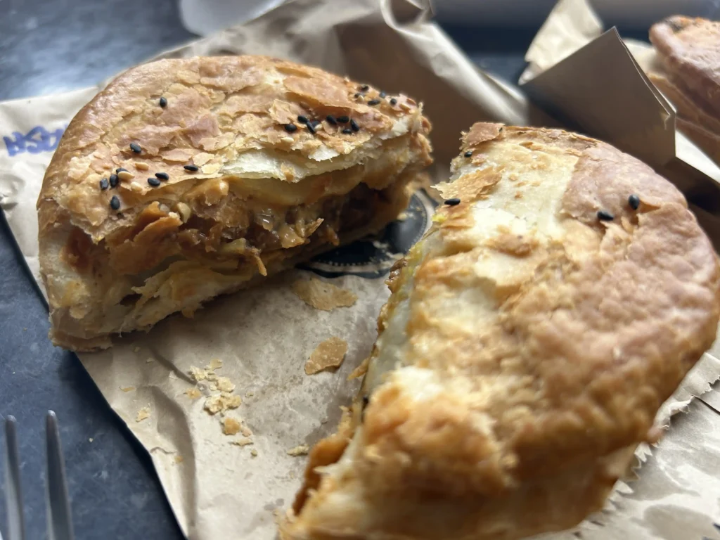Sanga's Pies Cromwell — flaky pastry pie with black sesame seeds and pulled meat filling, cut open on Sanga's Pie Co branded wrapper
