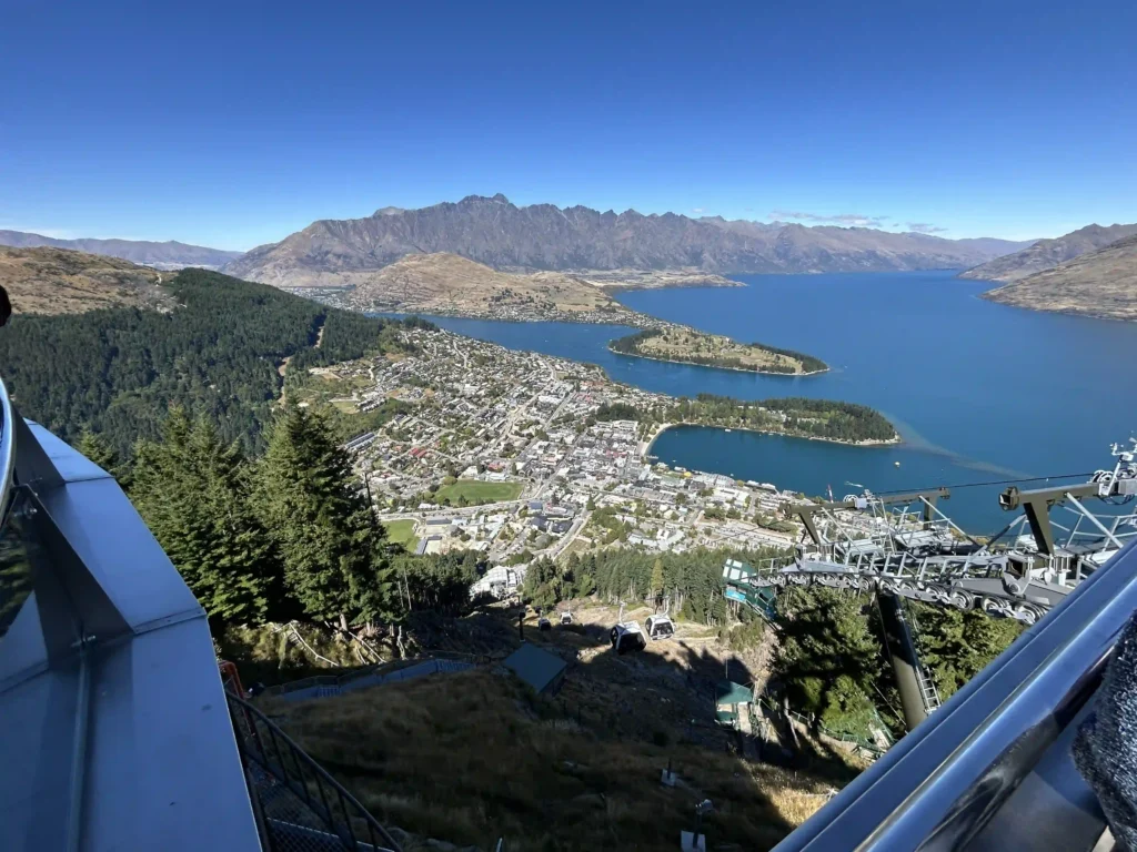 View from the top of Queenstown Skyline Gondola — Queenstown town, Lake Wakatipu and The Remarkables spread out below on a clear blue sky day
