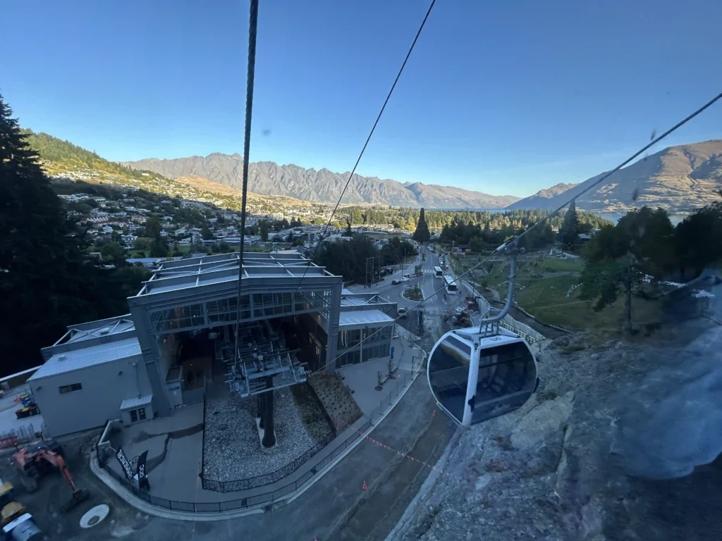 Queenstown Skyline Gondola cabin approaching the lower terminal at dusk — Queenstown residential area and lake visible through the gondola window